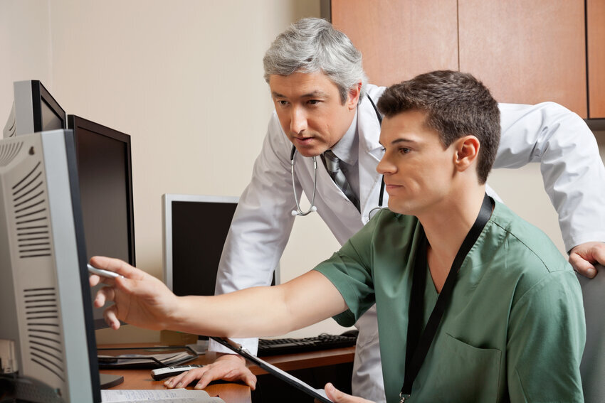 Medical assistant points to computer monitor as physician looks