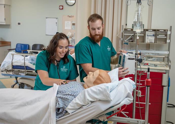 Nursing student standing next to instructor, smiling at a nursing simulation mannequin